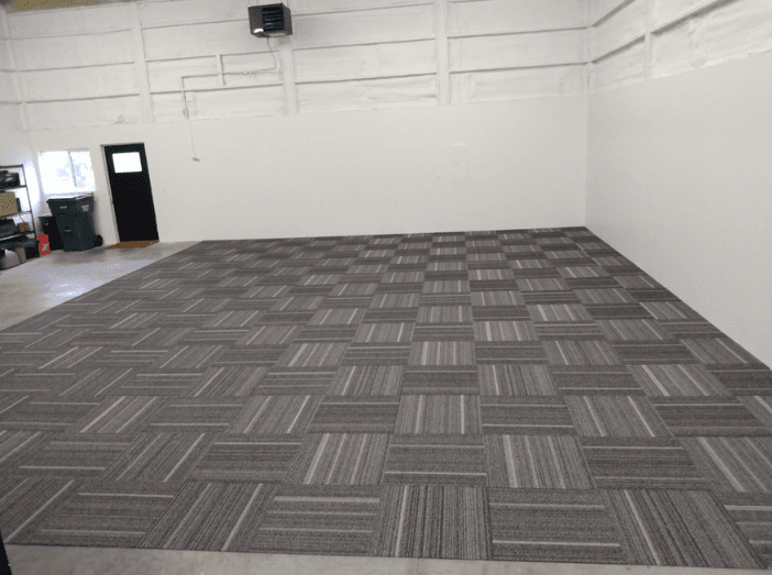 Second view of the same gray carpet tile floor showing its straight perimeter edge and alternating tile direction