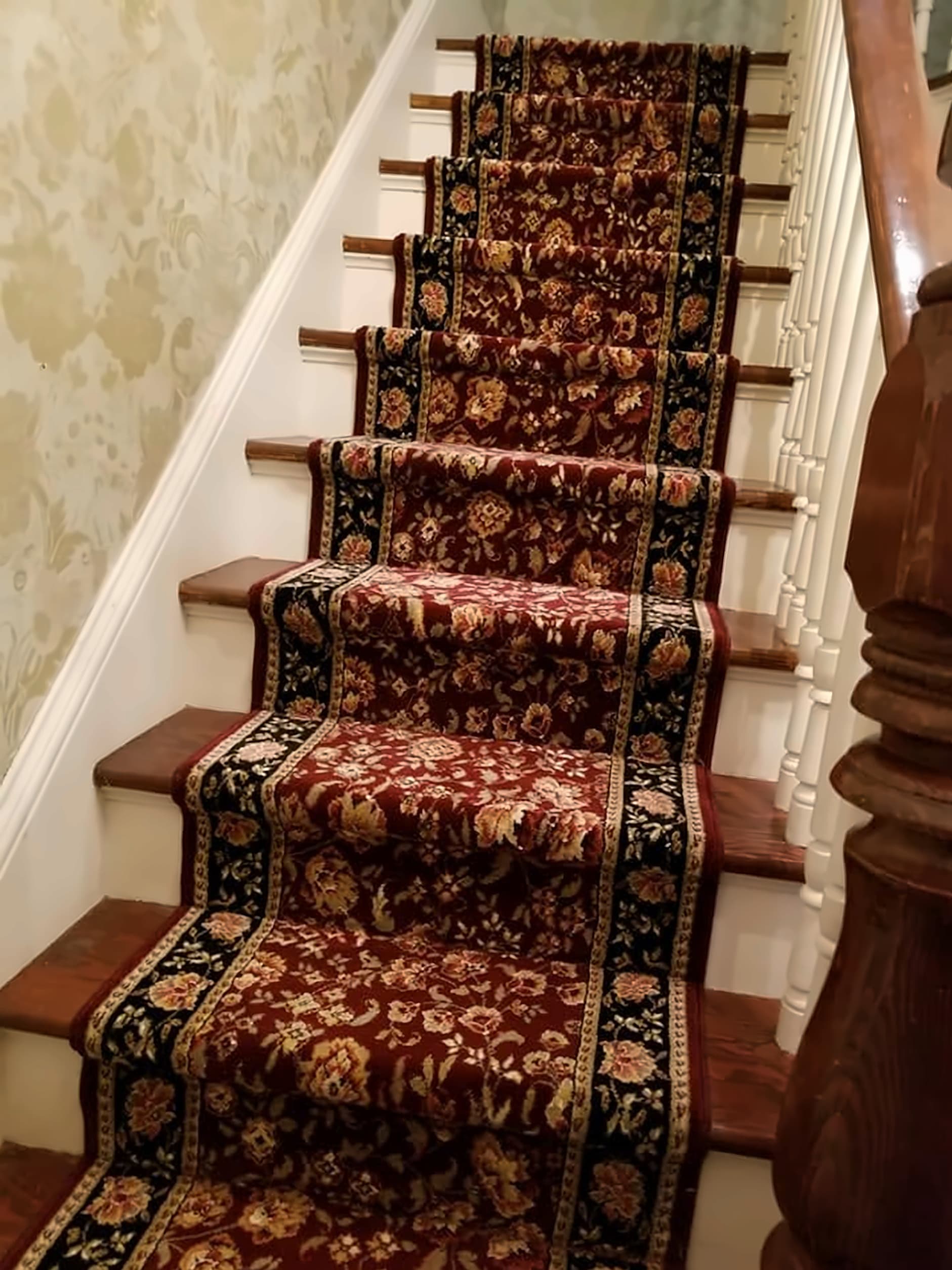 Red and black patterned stair runner installed on a wood staircase beside a turned newel post