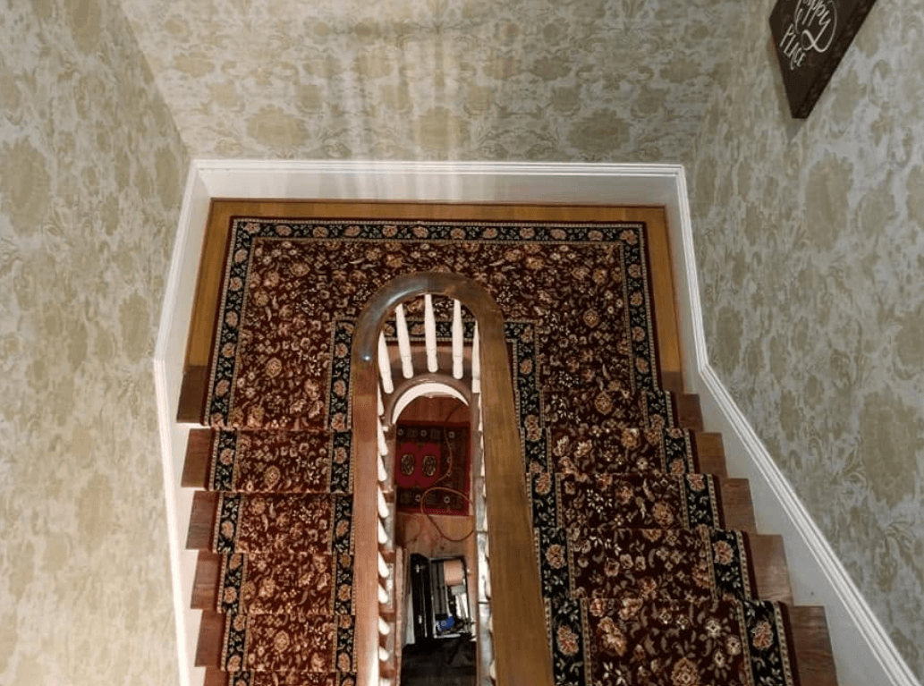 View down a stairwell of a red patterned runner wrapping a landing